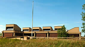 large building with tall grass in the foreground and flag pole next to building large building with tall grass in the foreground and flag pole next to building