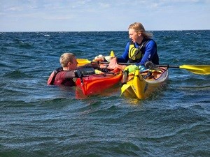 Kayaker assisting another kayaker who is in the water holding onto their kayak.