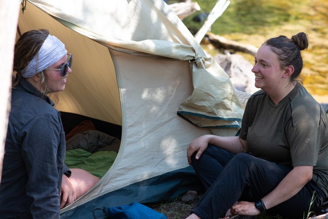 Two people in conversation sit near a tent.
