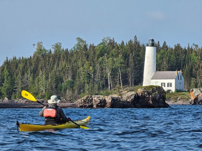 A man kayaking in front of Rock Harbor Lighthouse on a sunny day.