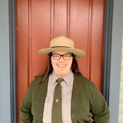 NPS Ranger standing in front of a red door while smiling