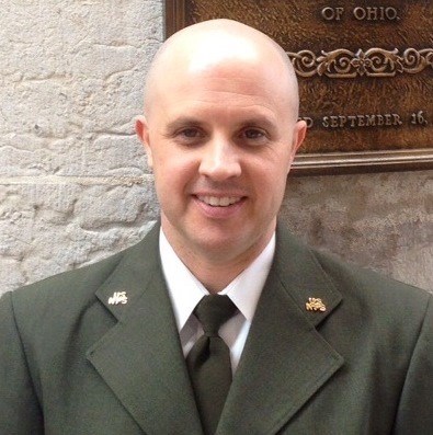 man standing in front of a stone wall and he is wearing a green suit jacket