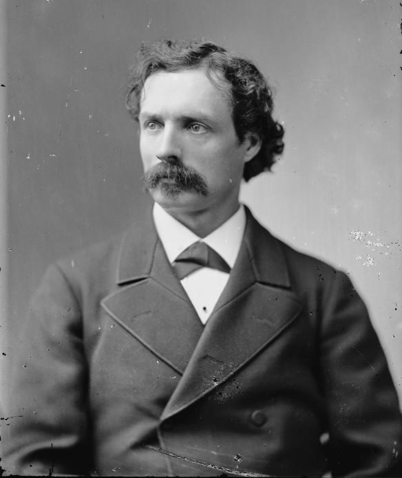 a man wearing a suit with a brown mustache is sitting