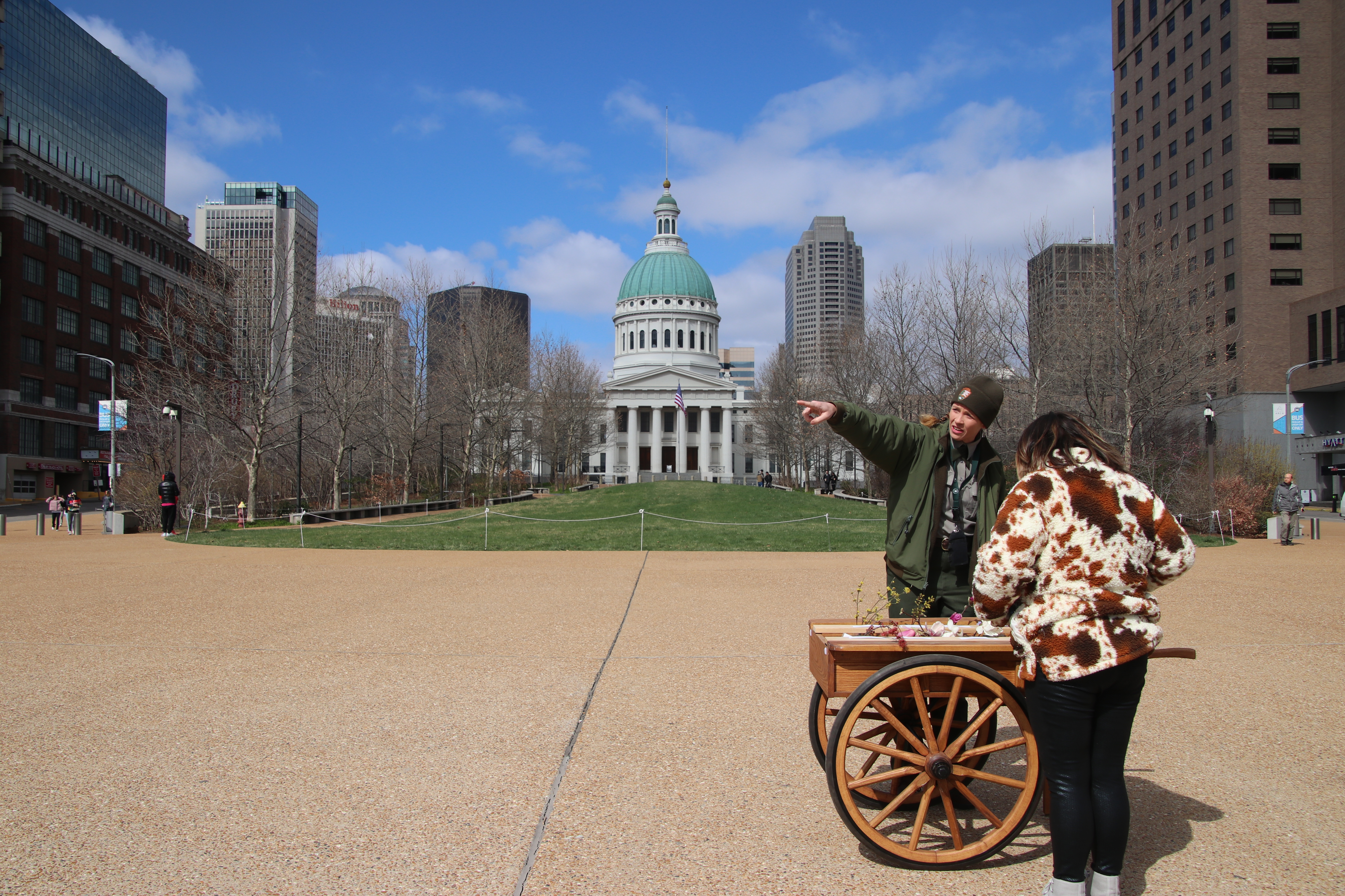 A woman looks down into a wooden cart filled with flowers as a park ranger points to the distance.