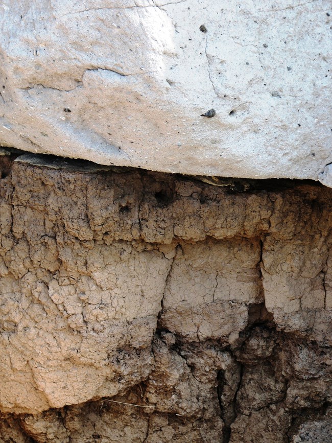 A whitish-gray rock rest atop a red-brown rock full of cracks.