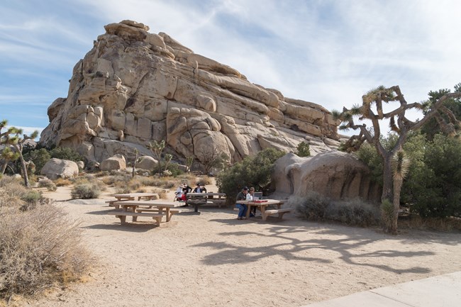 Visitors sit at picnic tables surrounded by large rock formations.