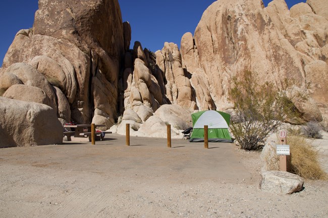 A green tent sits on a paved campsite platform next to rock formations