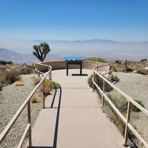 Paved sidewalk leads to viewpoint of mountains with an educational sign and map.