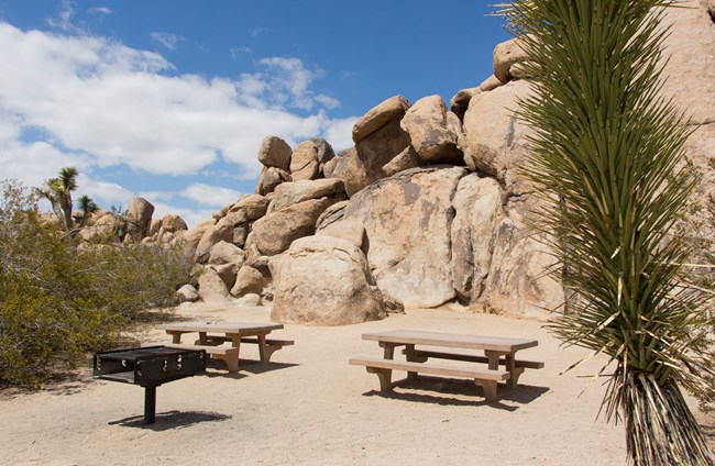 Picnic tables and a grill surrounded by large rocks.