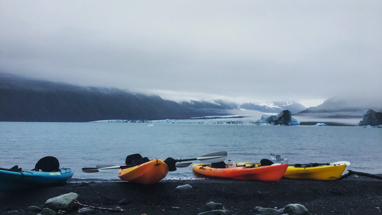 Four kayaks on shore with a glacier in the distance