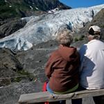 A couple sits on a park bench, viewing the nearby Exit Glacier.