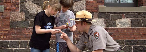 A ranger and two young visitors look at some rocks for copper.