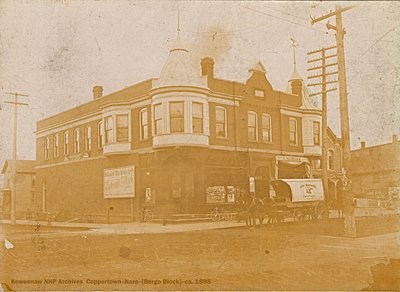 A building is situated on a corner of two streets with a horse-drawn wagon out front.