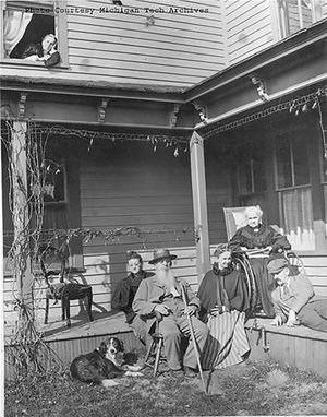 Five people and a dog sitting outside on the front porch of a house.