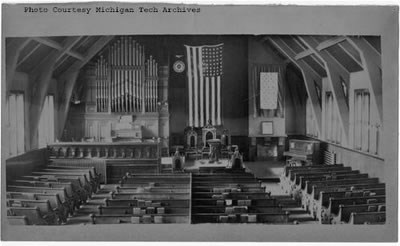 The interior of a church with lines of pews and an American flag hung up at the front.