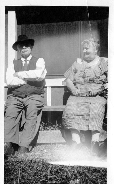 A man and woman sit on a porch situated on the front of a house.