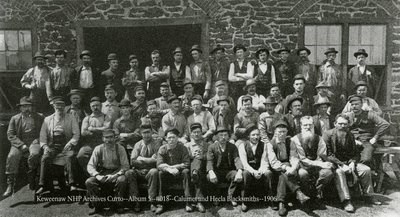 A large group of men pose for a photograph outside of a masonry structure.