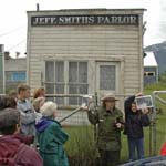 A female ranger holds a photograph for a group to compare with historic building behind her.
