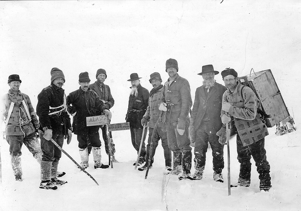 Nine men stand at the Alaska British Columbia border in the snow