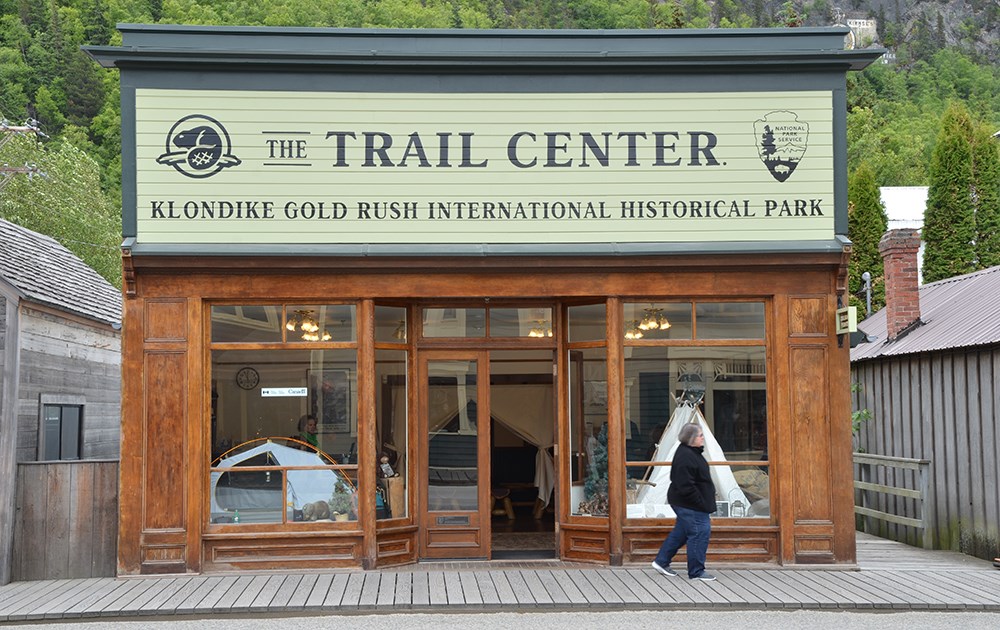 A building with large windows displaying a modern and historic tent.  A large sign reads "The Trail Center" with NPS and Parks Canada logos