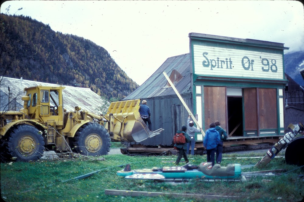 large machinery approaches a small building with large sign "Spirit of '98"