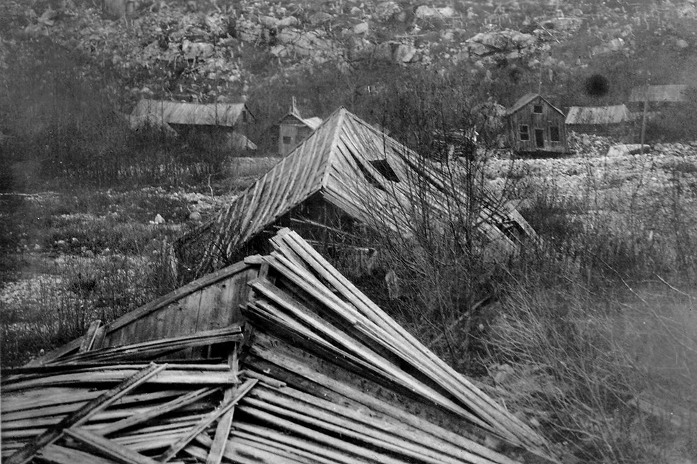 Black and white photo of collapsing buildings in rocky brush area