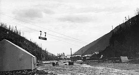 Historic photo of an item on a tram line flying over a rough valley camp.