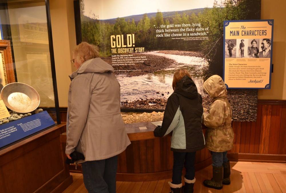 An adult and two children look at museum exhibits.