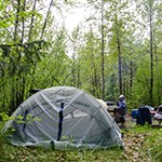 A tent in a forested area with people in the background