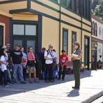 A ranger talks to a group of people next to brightly colored buildings
