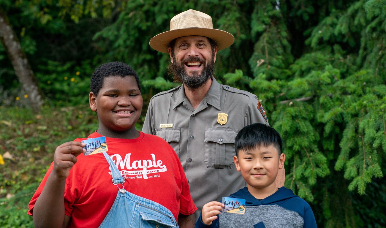 A ranger poses with two children holding up park passes.