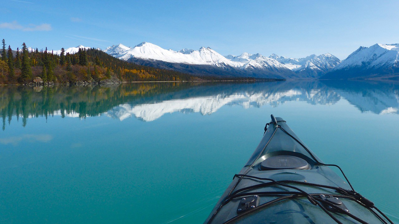 A kayaker's view of mountains reflecting in a calm turquoise lake
