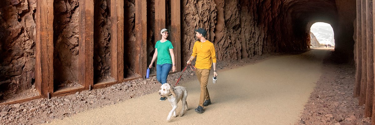 Two hikers with a dog walk through railroad tunnel on Historic Railroad trail