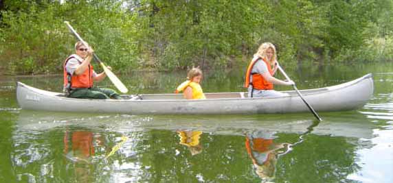 Ranger leading a guided-canoe trip. A ranger with two visitors sitting in a canoe paddling on the water.