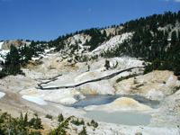 View of Bumpass Hell boardwalk winding through thermal areas with grey and yellow thermally altered earth.