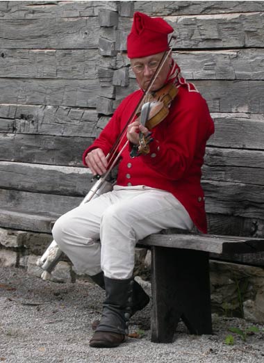 Fiddler, in red coat and hat, playing at Fort Osage.