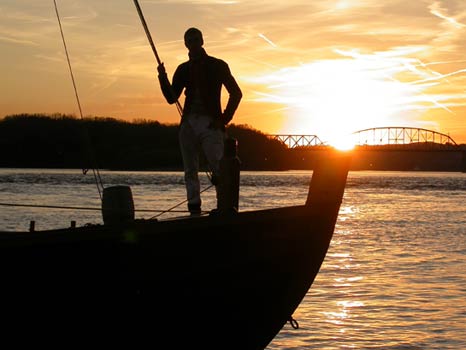 Silhouette of man and keelboat on Ohio River with sun setting behind.