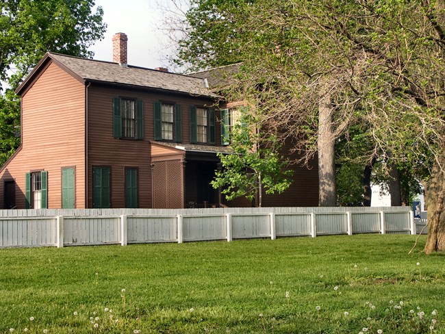 The Dean House, a two story brown house with green shutters
