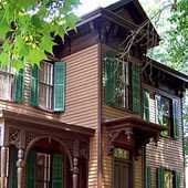Two story brown house with green shutters and a small side porch