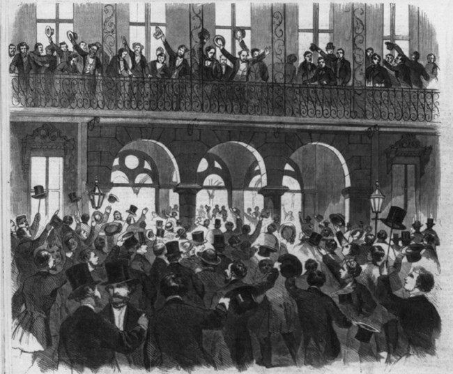 Crowd of men in a large hall cheering and throwing their top hats in the air on the inner balconies and main floor.