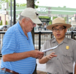 A young male ranger talking to a visitor while holding a piece of paper