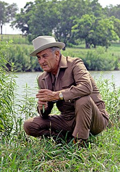Lyndon Johnson kneeling on the banks of the Pedernales River
