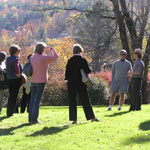A ranger speaks with a group of people on a sloping green lawn, lit by the waning afternoon light of a fall day.