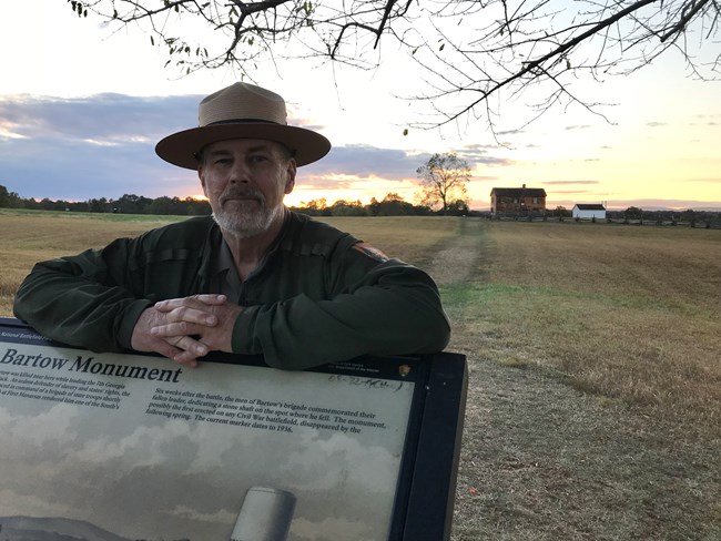 Ranger leans on a wayside with the sunset in the background.