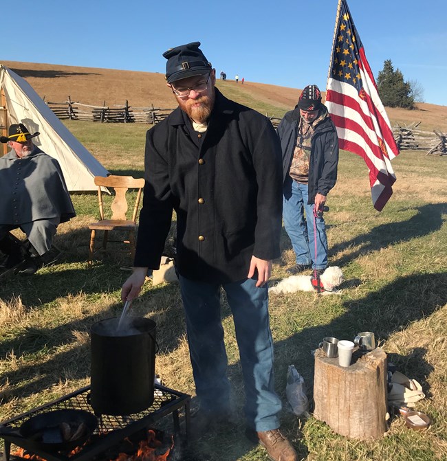 A living historian in union uniform stirs water.