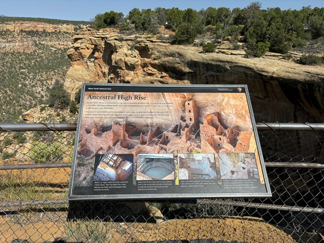 An image within a metal frame secure to a fence describes the ancestral site, not in the photo, but in the dark alcove in the canyon to the right of the sign.