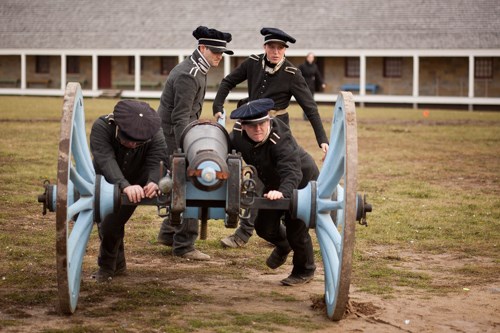 Re-enactors, dressed as 1820s soldiers, push a cannon.