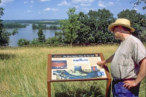 A man looks at an exhibit overlooking a lake.