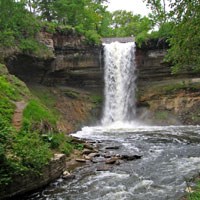 Minnehaha Falls drops over a ledge into a gorge surrounded by trees.