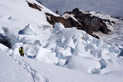 A roped-up climber ascends a snowy slope next to a section of glacier broken by seracs.